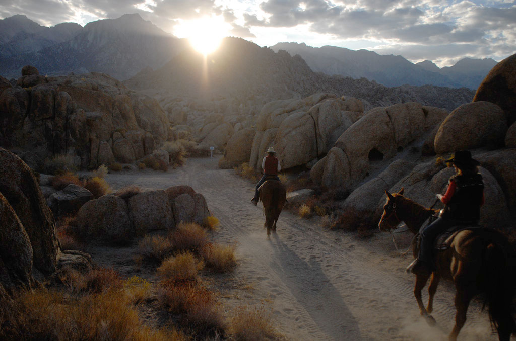 Two Riders riding on a trail through rocks into the sunset.